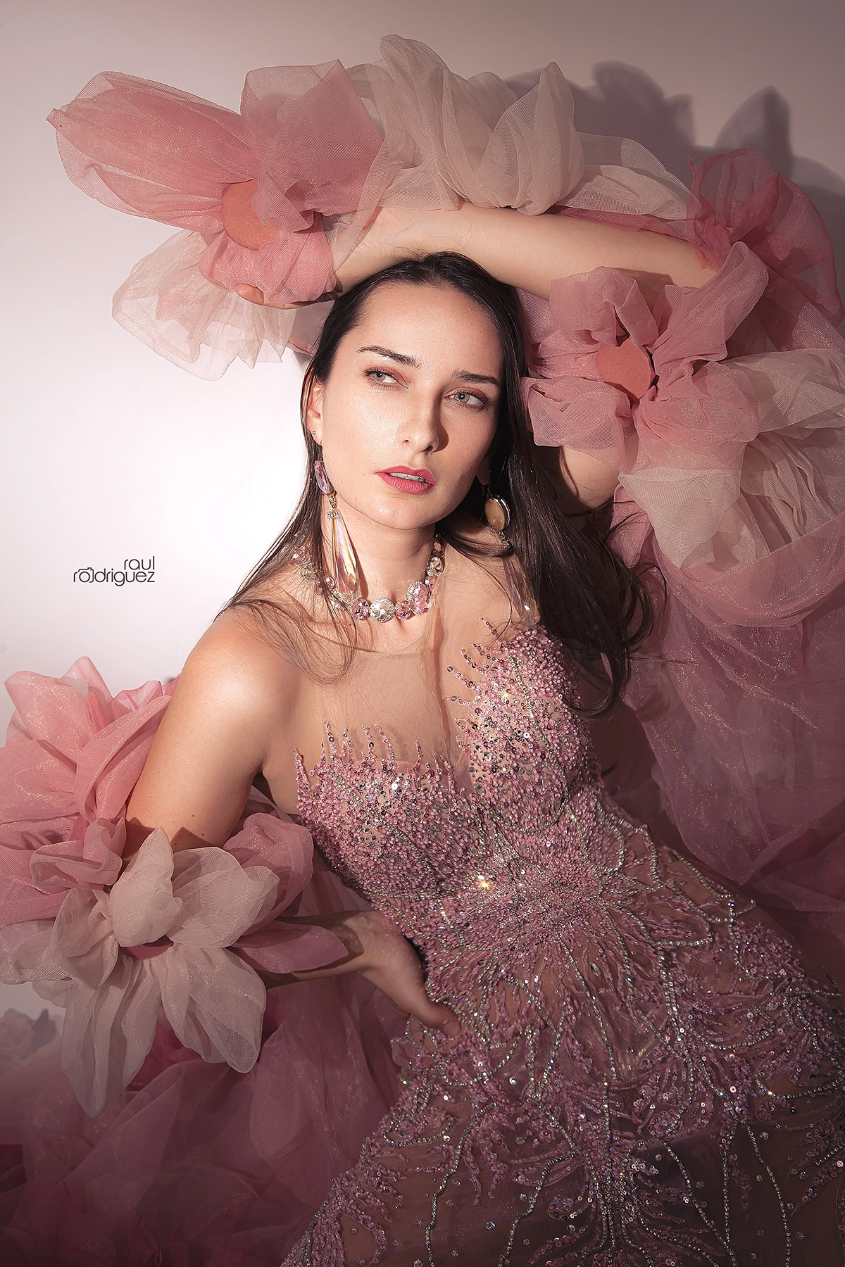 Retrato editorial con un brazo elevado sobre la cabeza, vestido rosa de pedrería y volúmenes de tul.