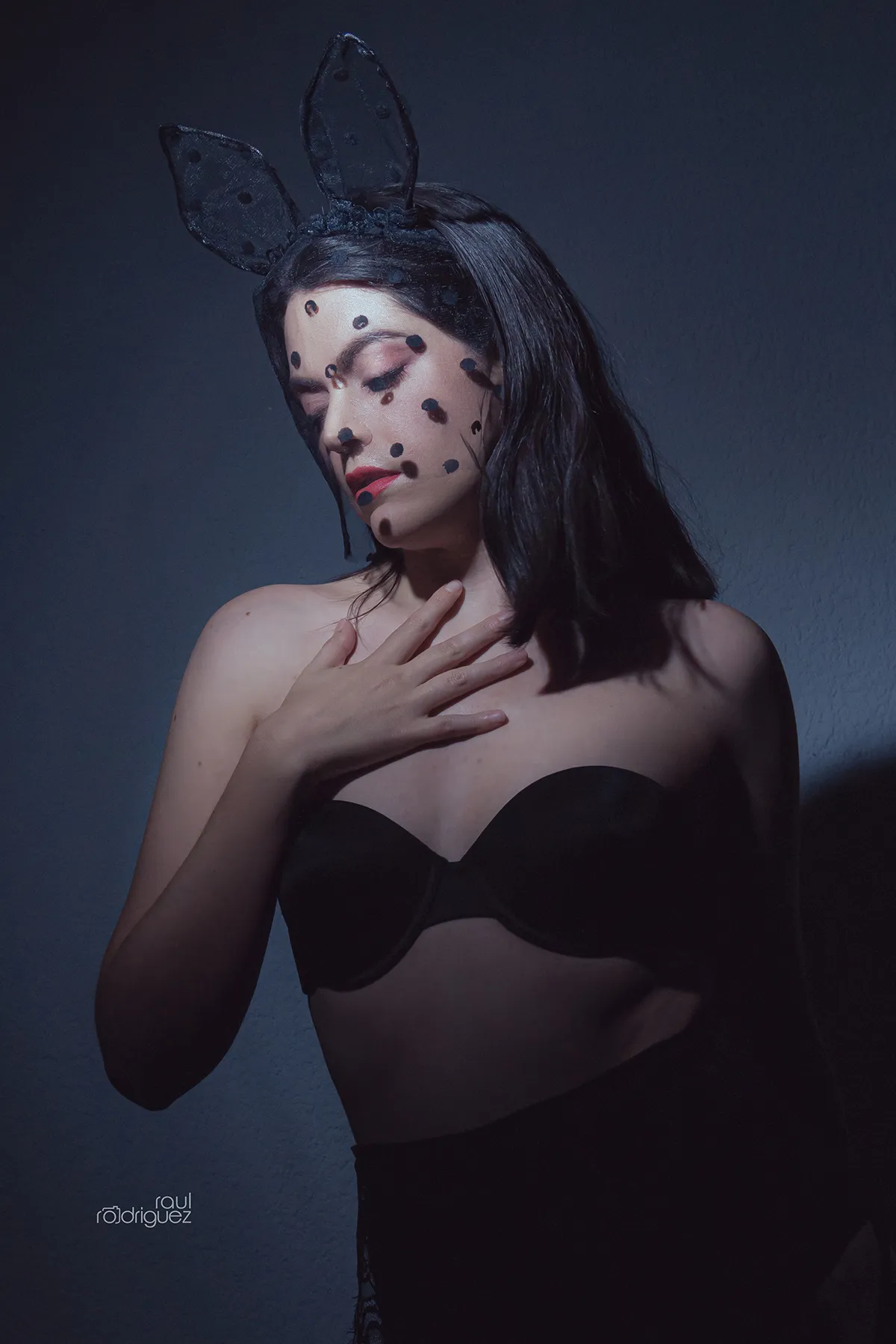 Retrato de mujer con orejas negras de conejo y velo de puntos, con la cabeza inclinada y una mano sobre el pecho.