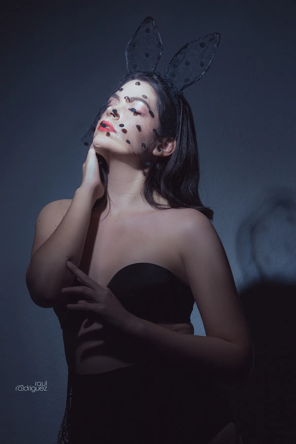 Retrato de mujer con orejas negras de conejo y velo de puntos, rostro inclinado hacia arriba y ojos cerrados.