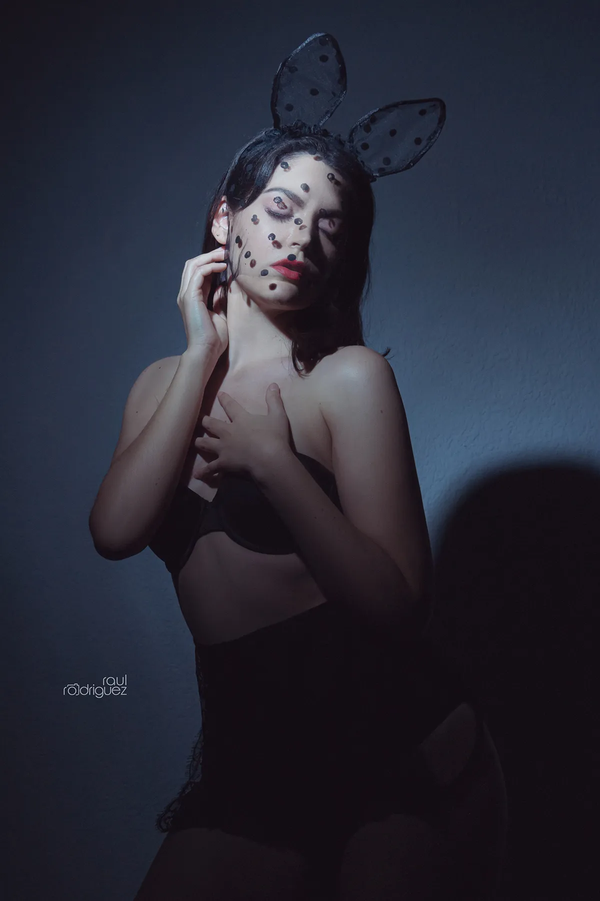 Retrato de mujer con orejas negras de conejo y velo de puntos, una mano junto al rostro y otra sobre el pecho.