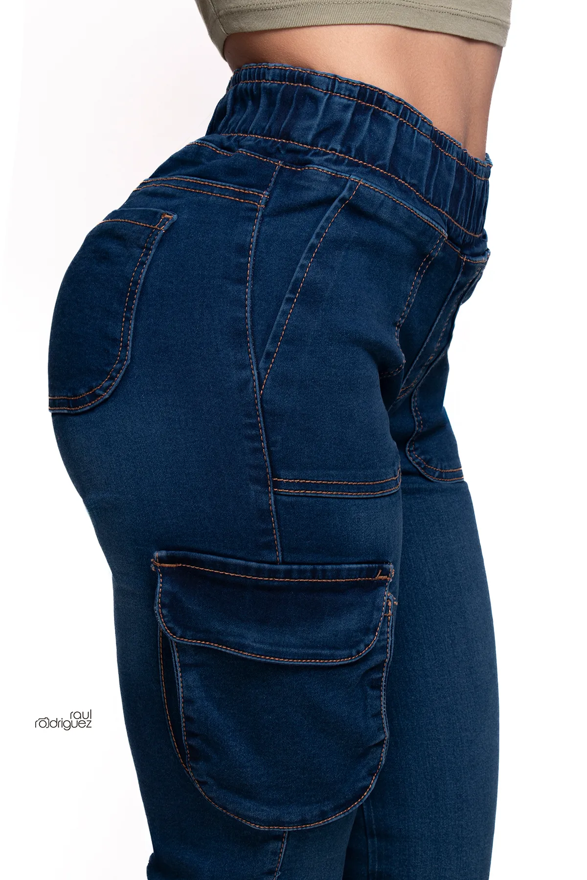 Acercamiento lateral a un pantalón cargo de mezclilla azul con cintura elástica, costuras contrastantes y bolsillos de solapa en la pierna.