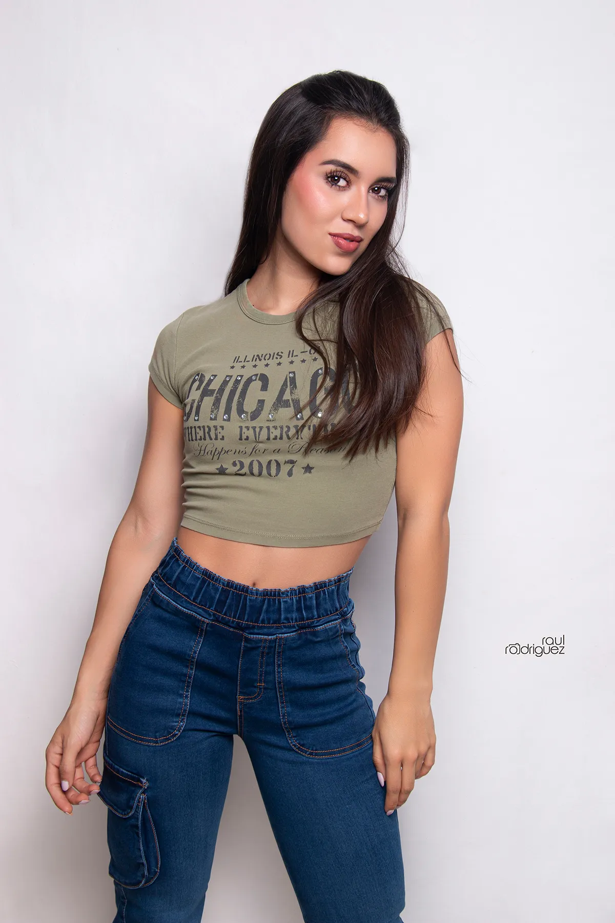 Mujer con camiseta corta verde y pantalón cargo de mezclilla azul posa de frente sobre fondo gris claro; se ven la cintura elástica y los bolsillos delanteros.