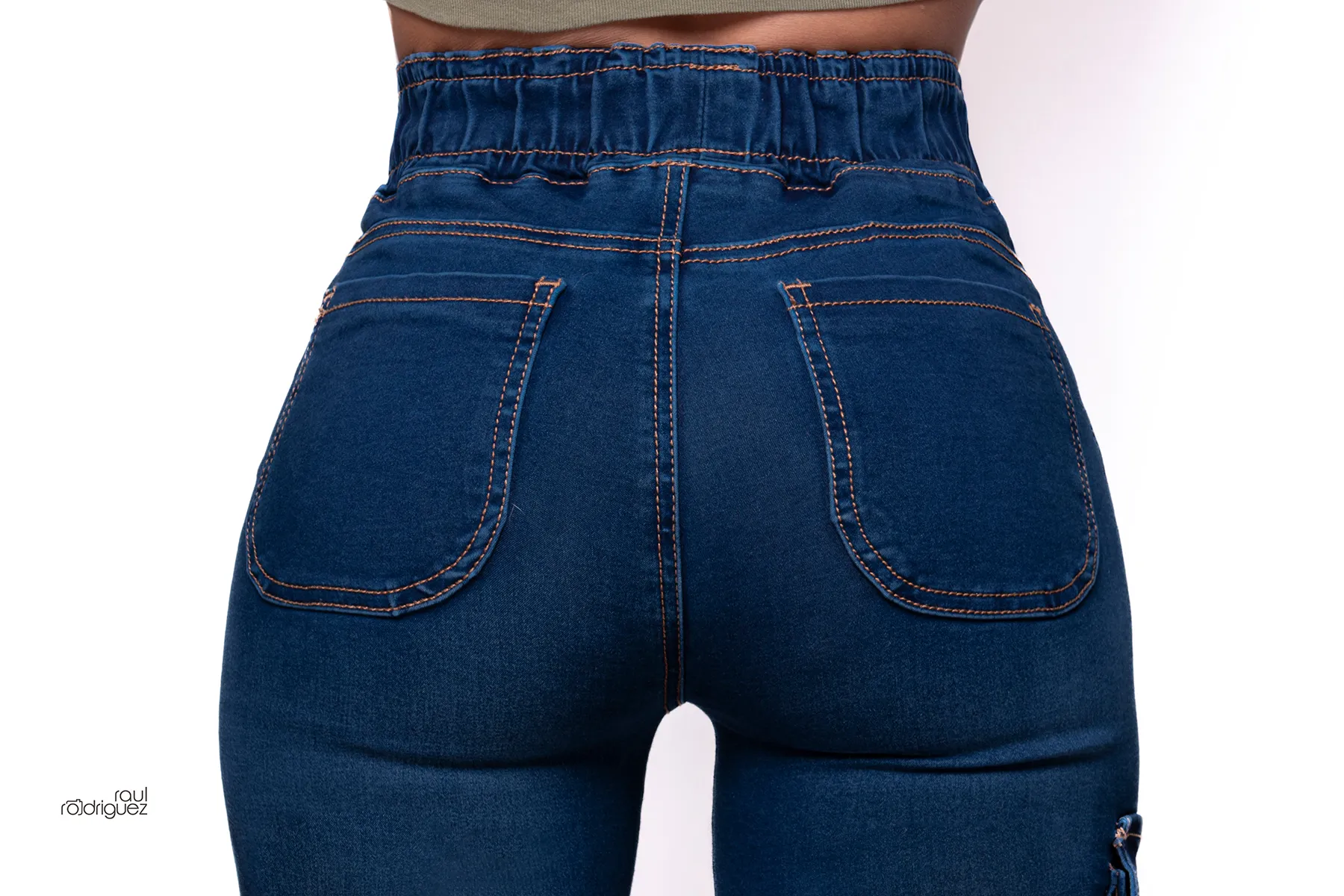 Acercamiento posterior a un pantalón cargo de mezclilla azul con cintura elástica, dos bolsillos traseros y costuras contrastantes sobre fondo blanco.