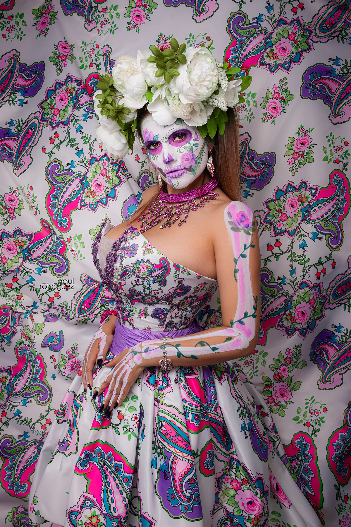 Retrato con maquillaje de calavera, tocado de flores blancas y vestuario estampado floral.