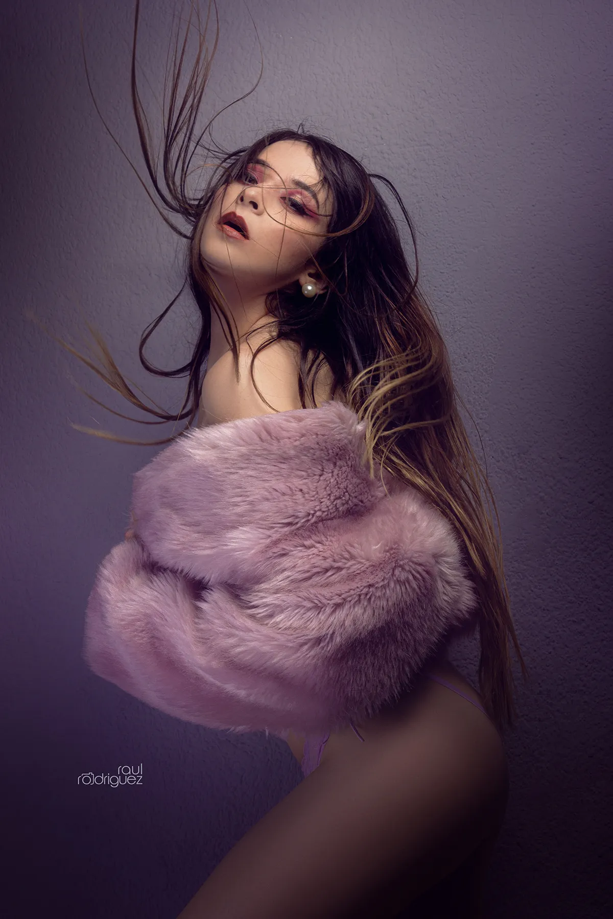 Mujer con abrigo de textura rosa y cabello en movimiento sobre fondo violeta.